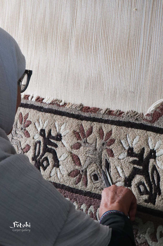 Craftsperson carefully tying knots on a traditional handmade rug with intricate floral design